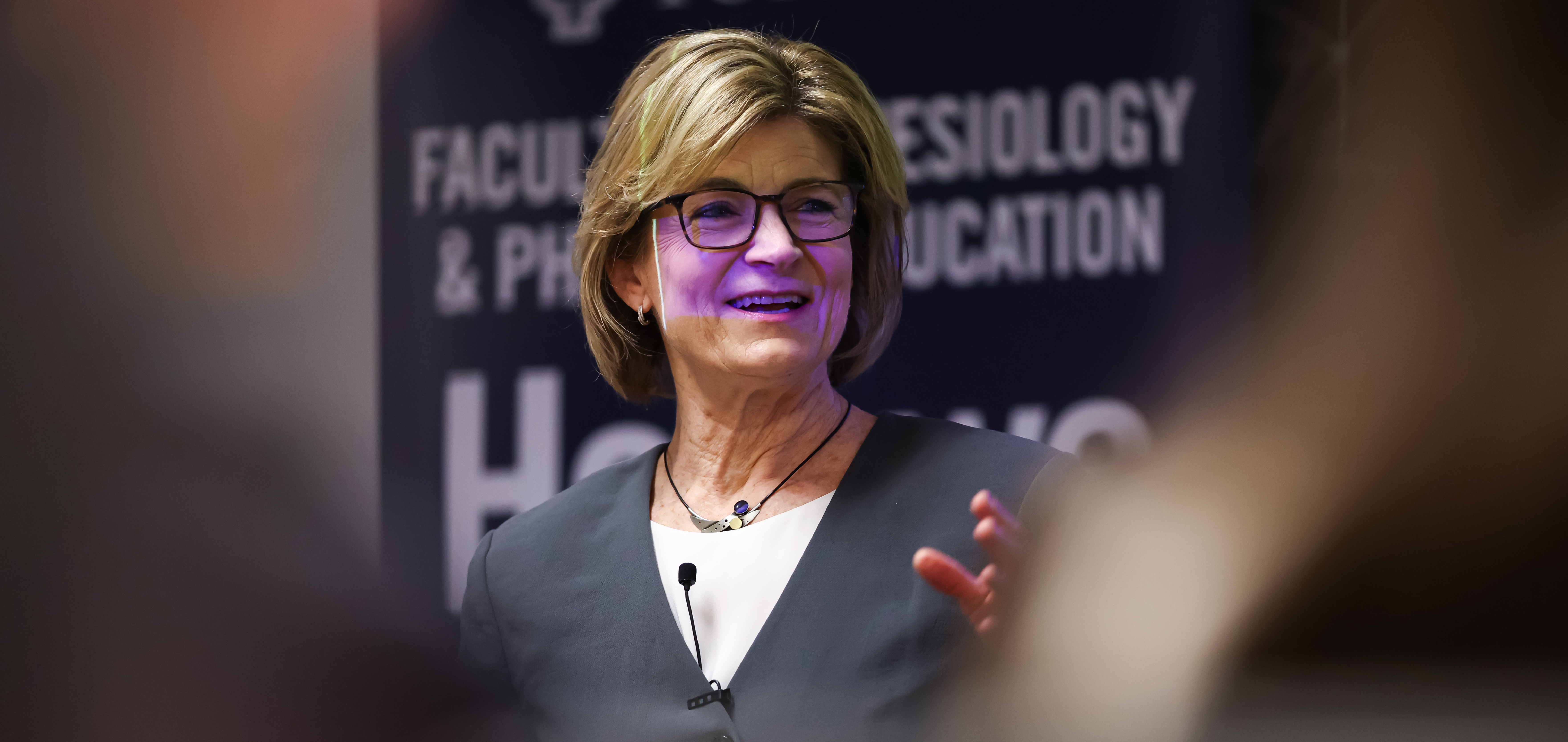 KPE dean professor Gretchen Kerr speaks at the National Undergraduate Research Conference in March 2025, standing in front of a KPE faculty banner