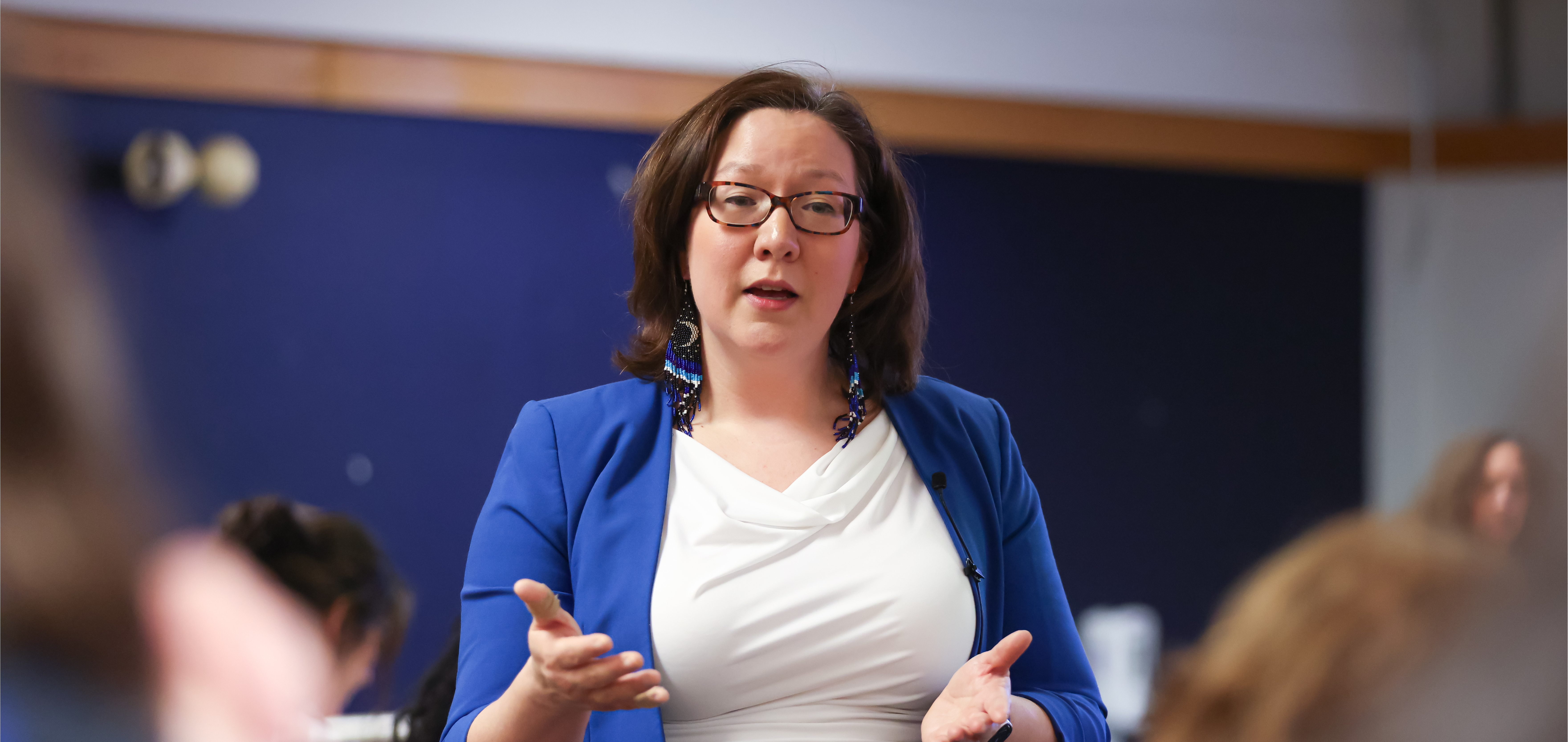 Dr. Tricia McGuire-Adams delivers a keynote at the National Undergraduate Research Conference, wearing a blue sweater and a white shirt