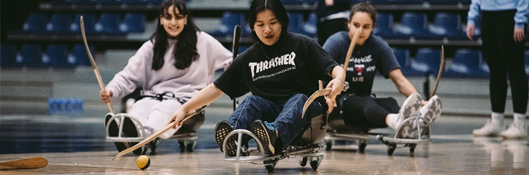 three students play an adapted hockey game using a sled