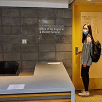 student in mask standing at entrance to KPE registrar's office
