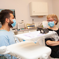 male health care provider in mask and scrubs chatting with patient in mask