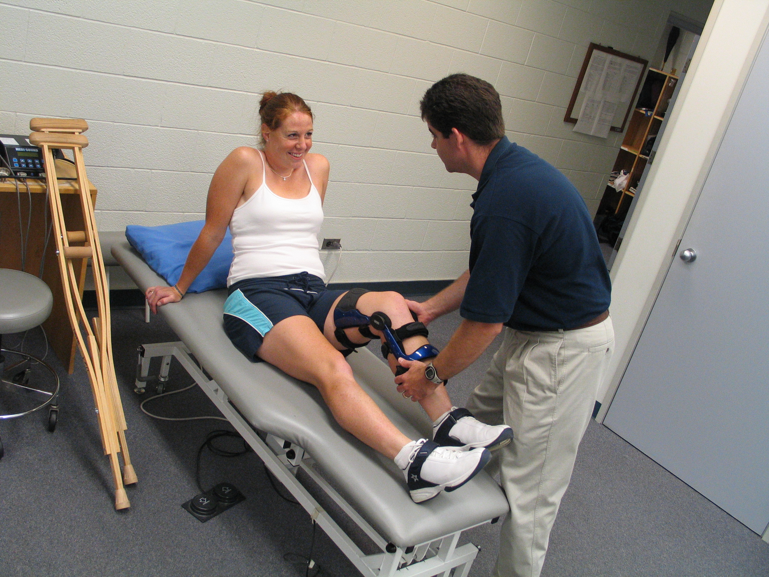 Therapist assists patient with knee brace and treatment in clinic