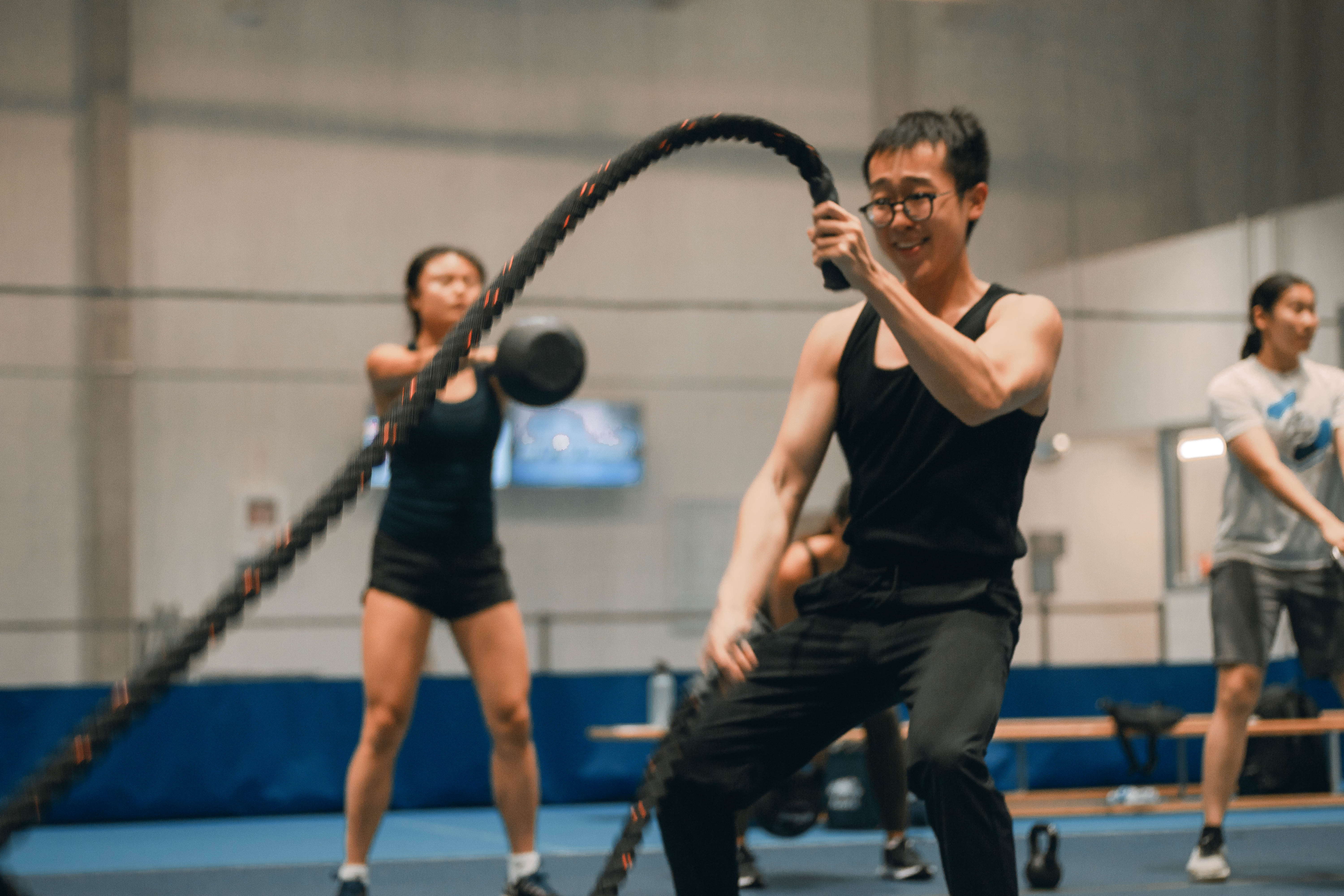 Man using battle ropes, 2 people swinging kettlebells in background