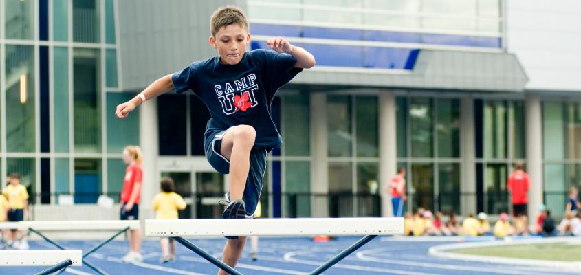 boy jumping over a hurdle on an outdoor track at Varsity Stadium