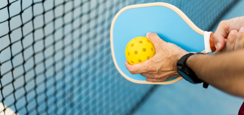 Person holding a pickleball ball up to a pickleball paddle