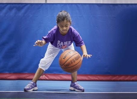A young camper practices dribbling a basketball